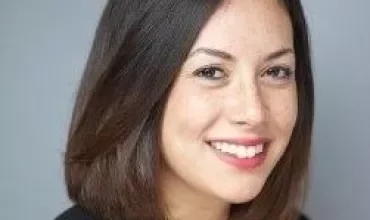 Smiling person with shoulder-length dark hair and a black jacket.