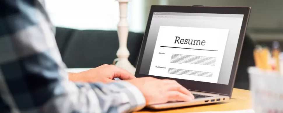 Person typing a resume on a laptop at a desk.