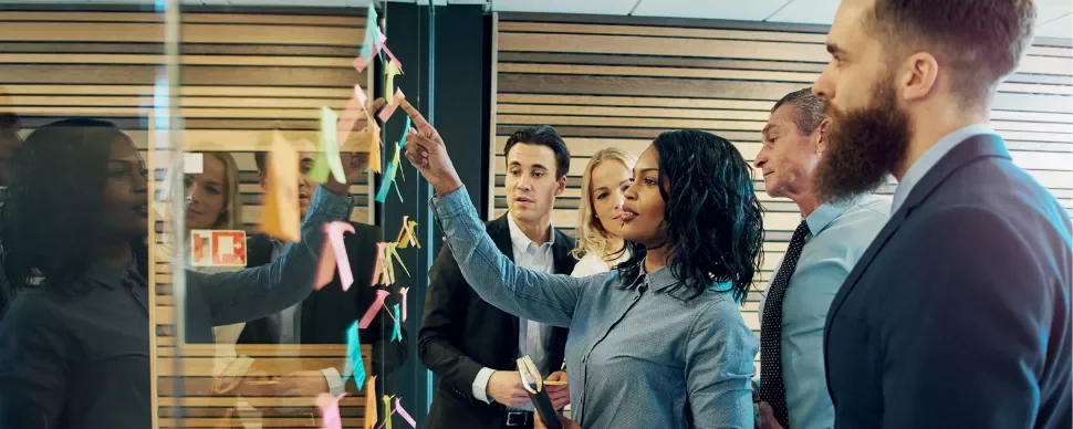Team discussing in front of a glass wall with sticky notes.