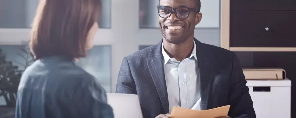 Two people having a meeting in an office setting, one holding a folder and smiling.
