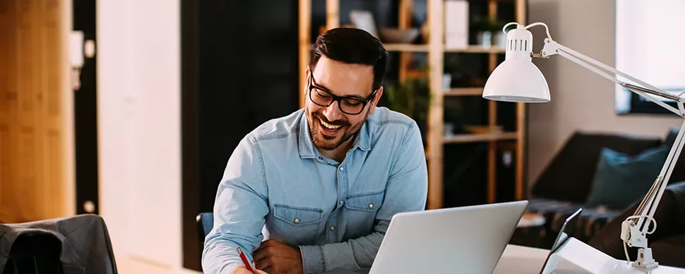 Man in a denim shirt working at a desk with a laptop.