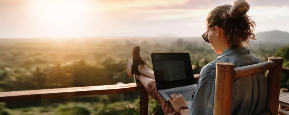 Person working on a laptop with a scenic view at sunset.