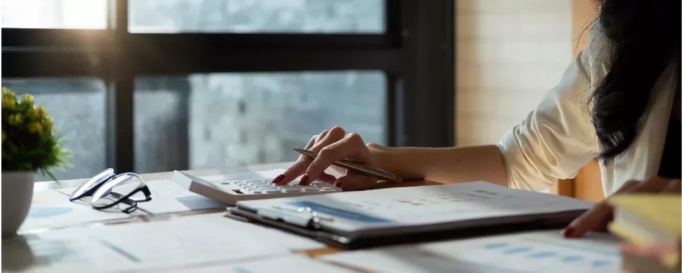 Person using calculator with papers and glasses on desk.