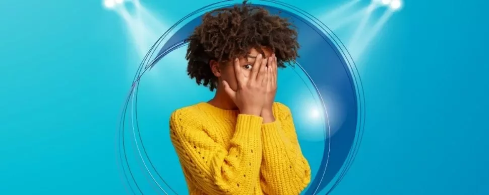Person in yellow sweater with hands over face against blue background.