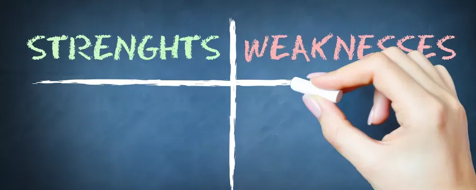 Hand holding chalk writes 'STRENGHTS' and 'WEAKNESSES' on a chalkboard grid.