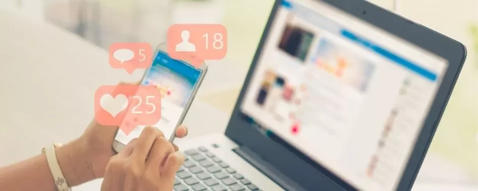 Person using a smartphone with social media notifications, next to a laptop.