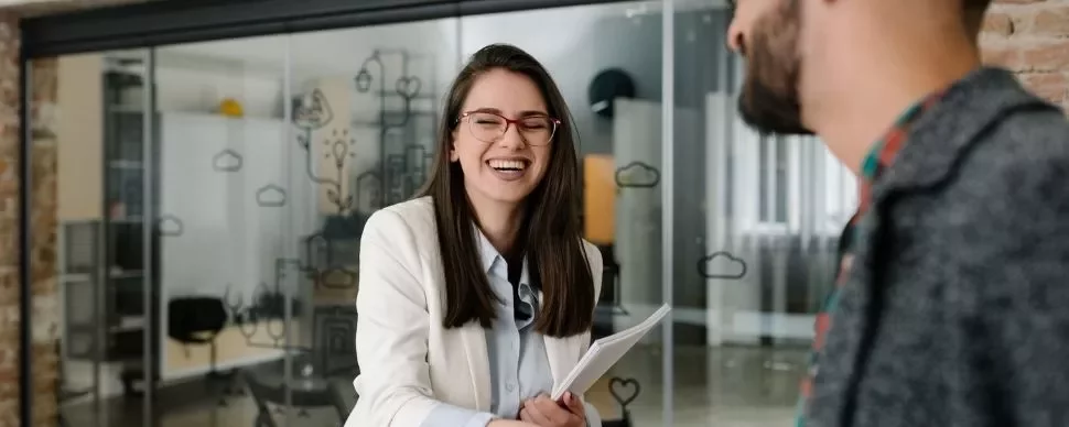 Woman in glasses smiles while shaking hands in a modern office.