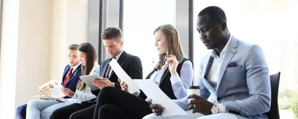 Business people seated in a waiting area, reviewing documents and tablets.