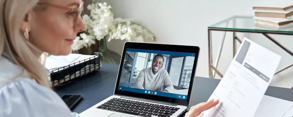 Woman video conferencing with a man, holding a resume.