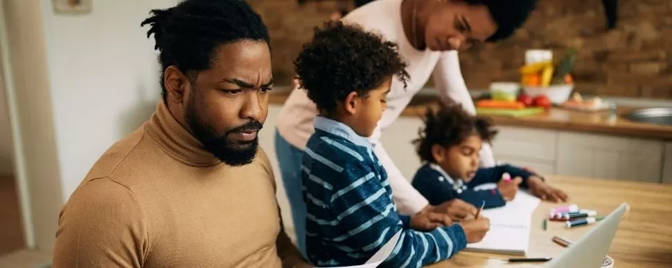 Family working together in the kitchen with a laptop and notebooks.