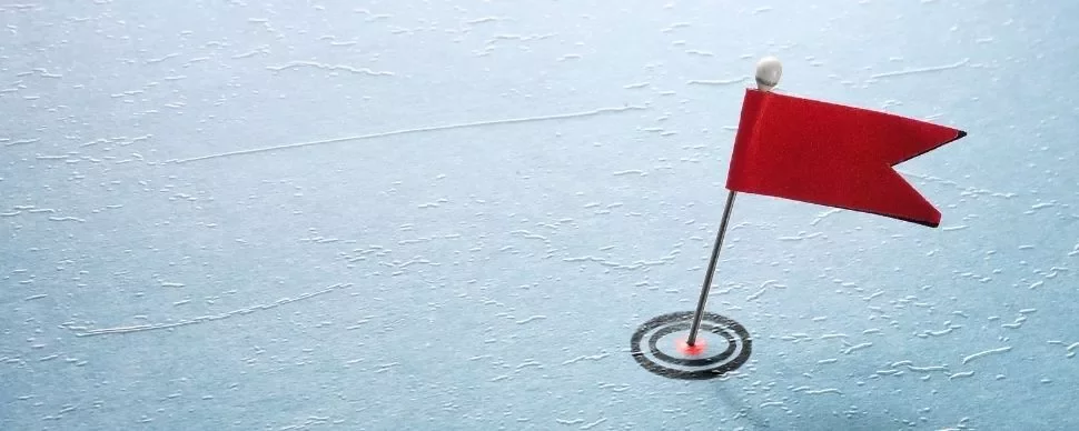 Small red flag on pin stuck into blue textured surface.