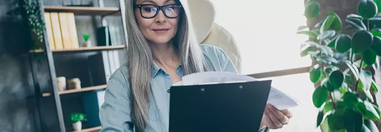 Woman with glasses reviewing documents at desk.