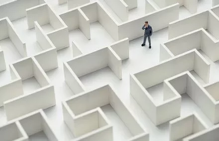 Person in suit standing in a large white maze, looking thoughtful.