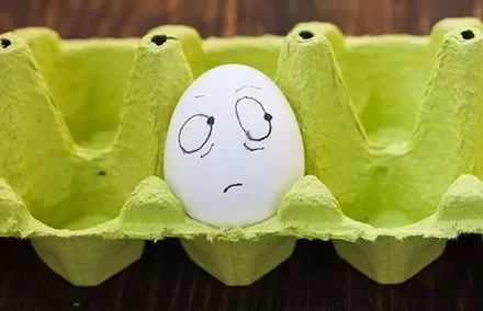 Egg with drawn face in yellow carton.
