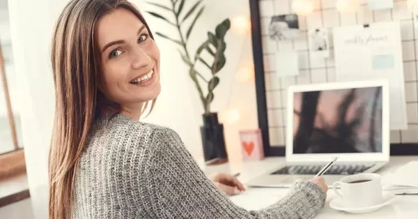 Smiling woman working at a desk with a laptop and coffee.