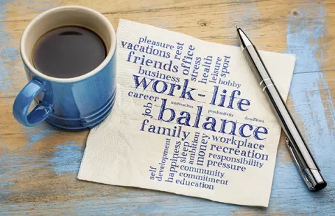 Coffee cup and pen next to napkin with 'work-life balance' word cloud.