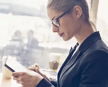 Woman with glasses reading a tablet in a coffee shop.