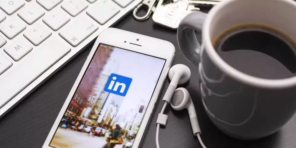 Smartphone displaying LinkedIn app next to a keyboard and coffee.