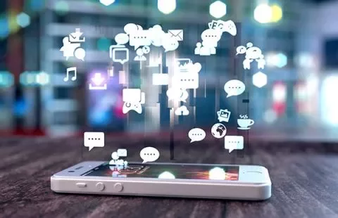 Smartphone with social media icons floating above it on a blurred background.
