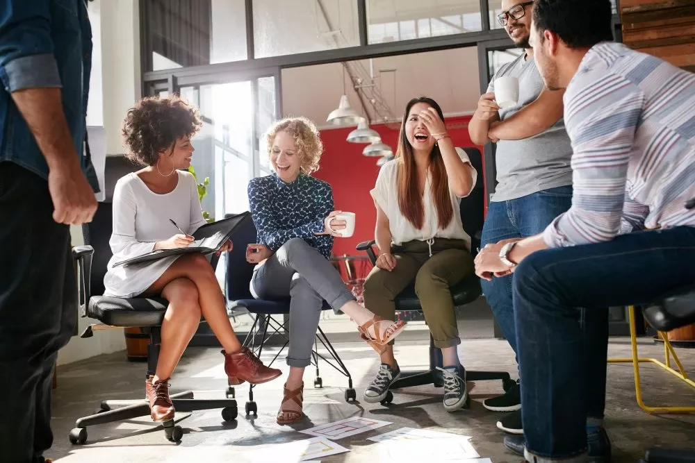 Group of colleagues laughing and talking in an office setting.