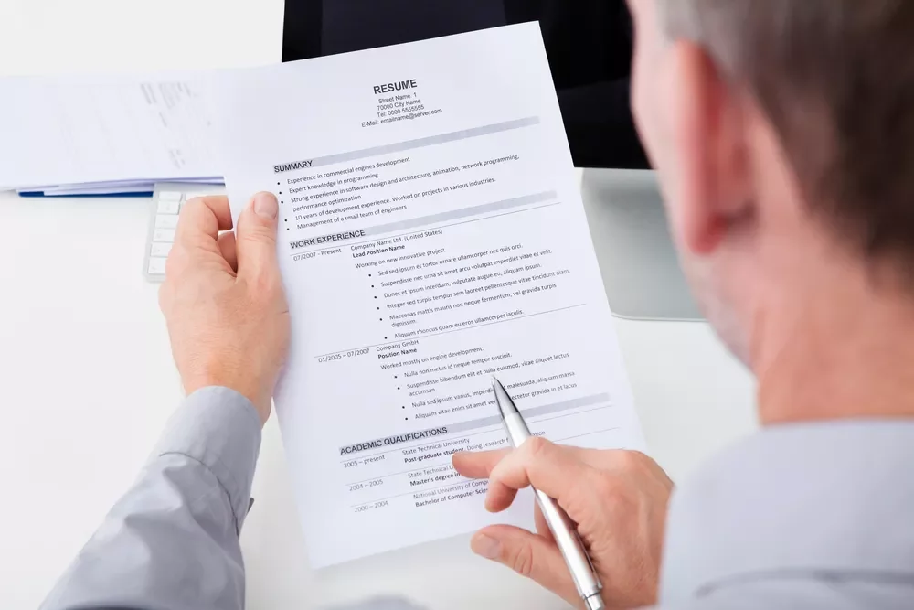 Person reviewing a printed resume with work experience and qualifications listed.