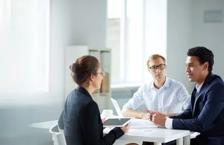 Three people having a meeting at a table in a bright room.