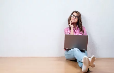 Woman sitting on floor with laptop looking thoughtful.