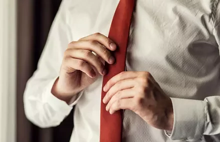 Person adjusting a red tie while wearing a white shirt.