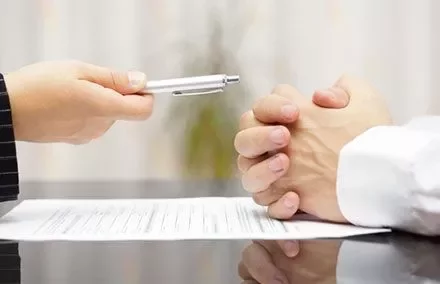 Two people at a table, one holding a pen over a contract document.