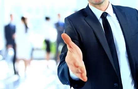 Businessman offering handshake, blurred office background.