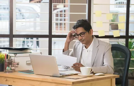 Man in office looking at document near laptop.
