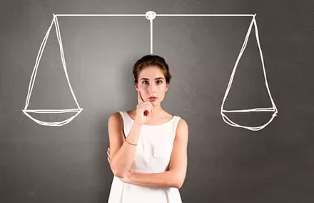 Woman contemplating in front of drawn balance scales on blackboard.