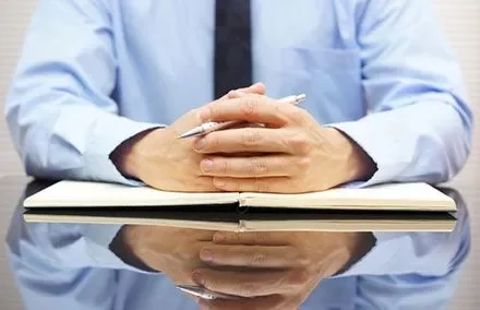 Person in a blue shirt with hands clasped over an open notebook on a reflective table.