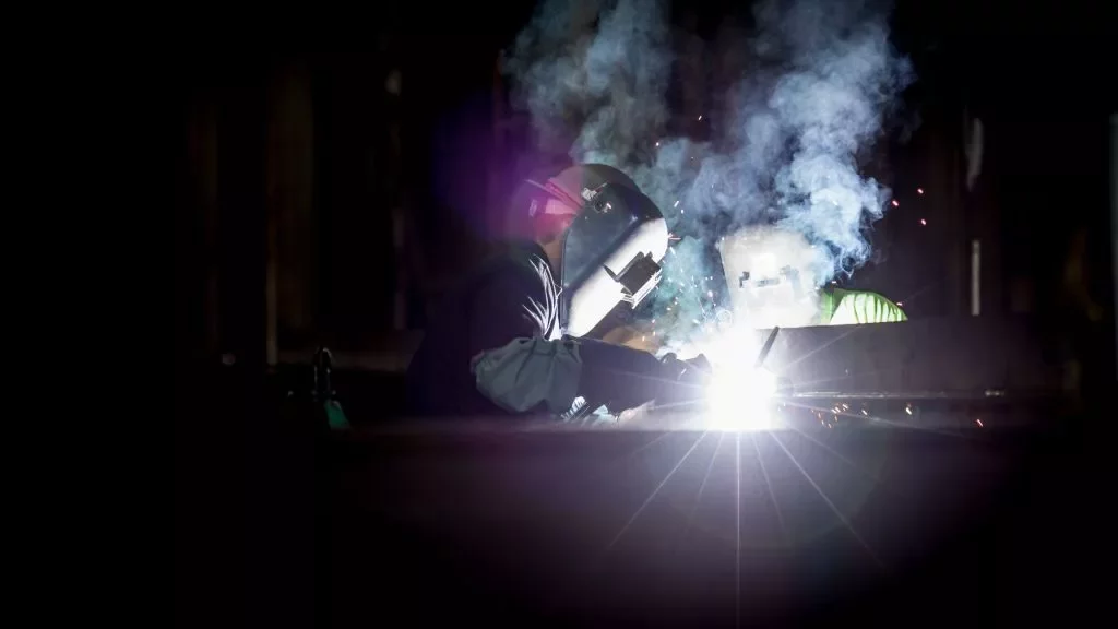 Welder working under a protective helmet with sparks flying.
