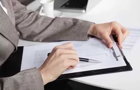 Person reviewing documents on a clipboard at a desk.