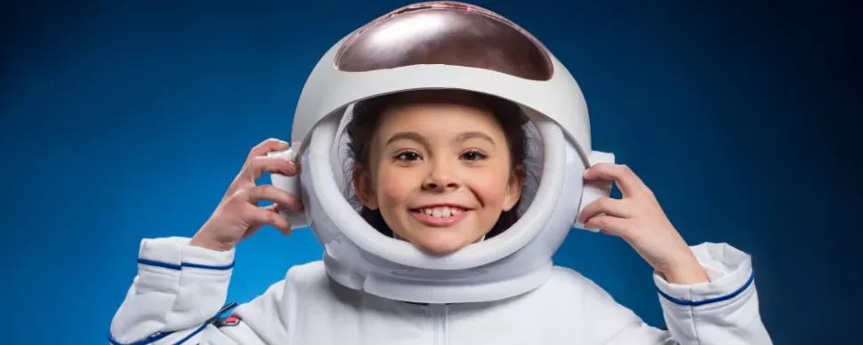 Child smiling in astronaut helmet against blue background.