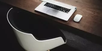 Laptop and mouse on wooden desk with modern chair.