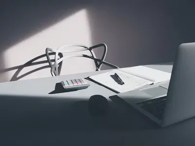 A laptop, notebook, pen, and calculator on a desk in sunlight.