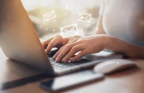 Person typing on a laptop with email icons floating above.