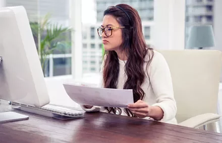 Woman at desk analyzing documents on computer.
