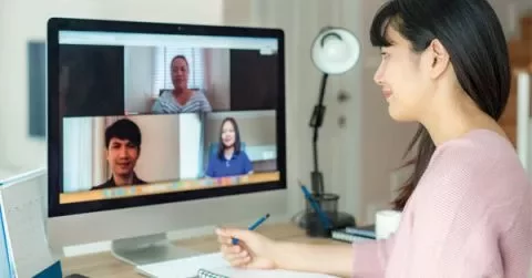 Woman participating in a video conference on a desktop computer.