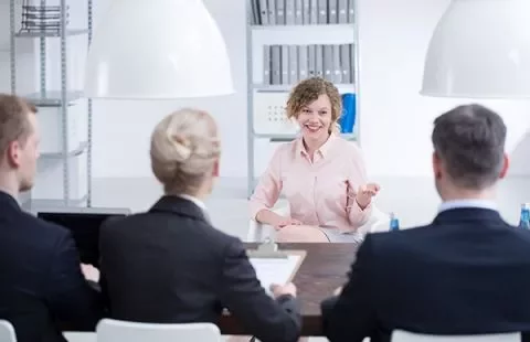Woman speaking to interview panel in office setting.
